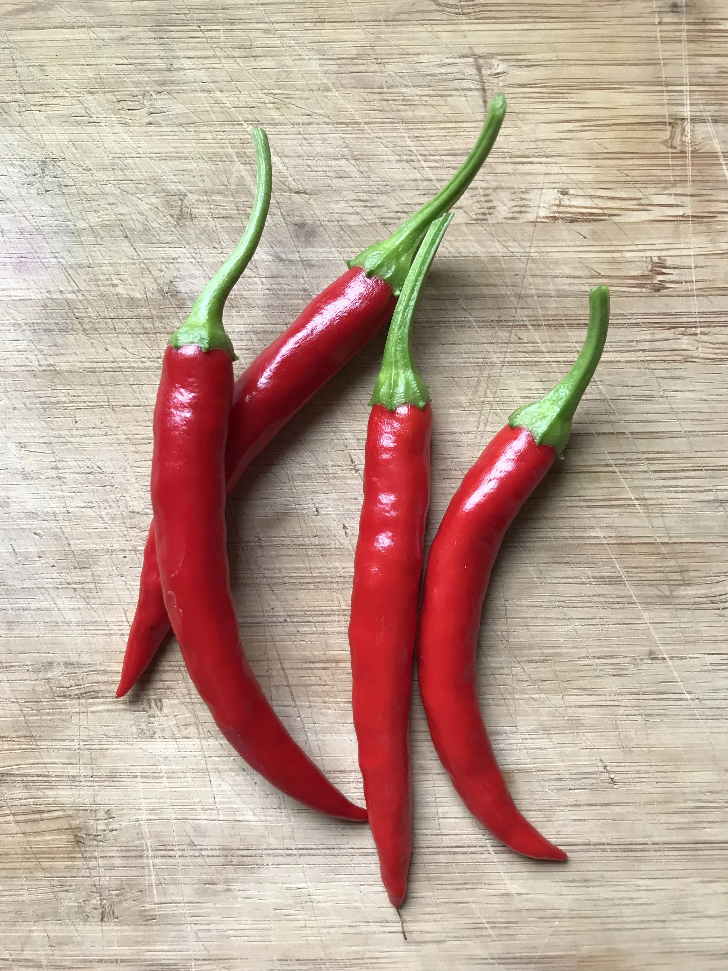 A close-up of three red chili peppers with green stems on a wooden cutting board.