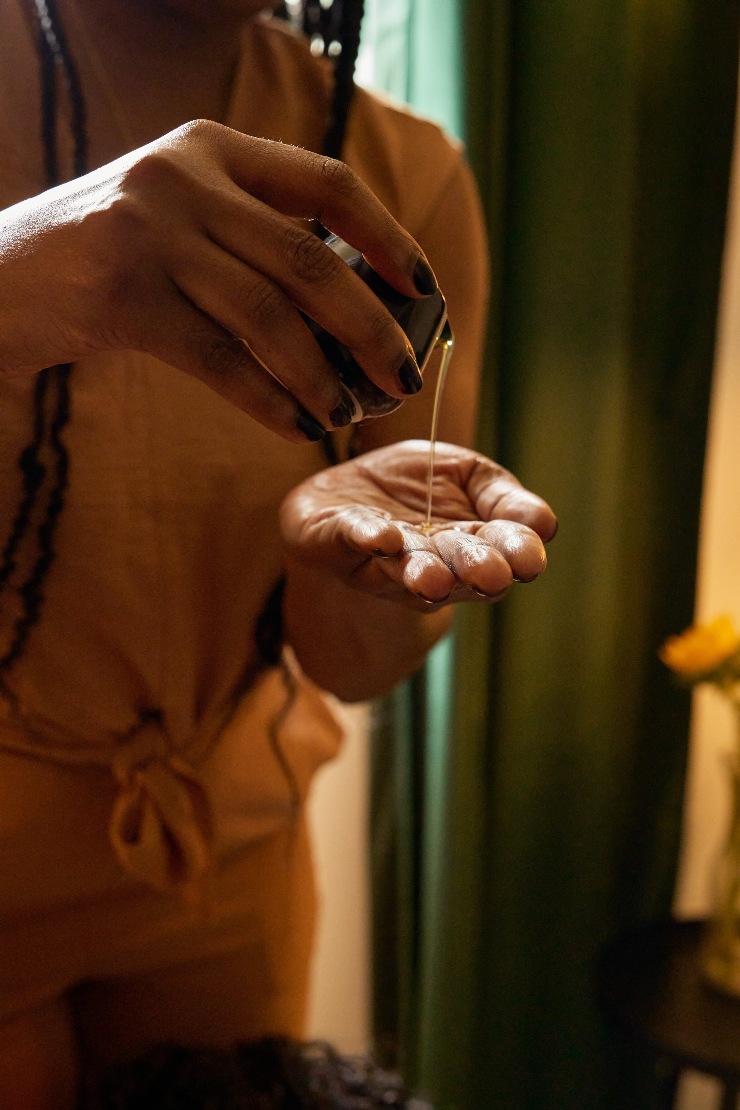 A person with dark skin pouring liquid from a small container onto their open hand in a dimly lit room.