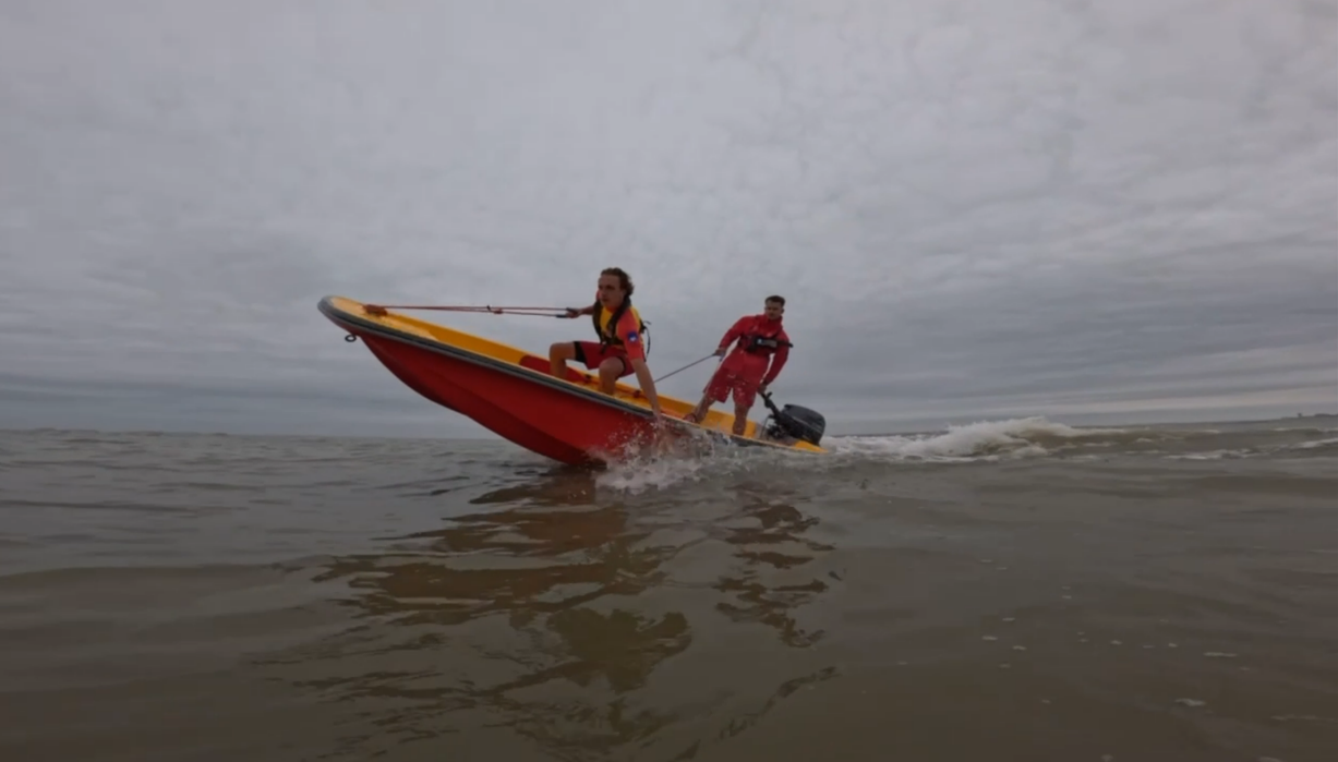 Two people on a small boat with an outboard motor, navigating on a body of water under cloudy skies.