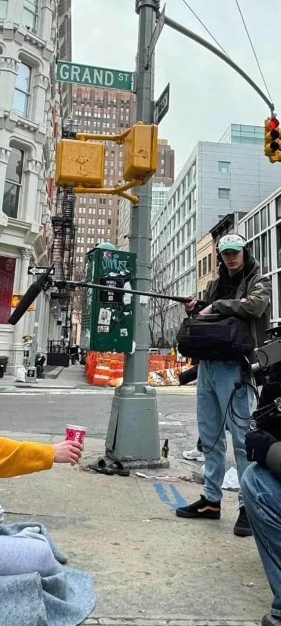 Street scene at the corner of Grand Street with a traffic light, a street sign, and a person holding a camera, surrounded by buildings in an urban environment.