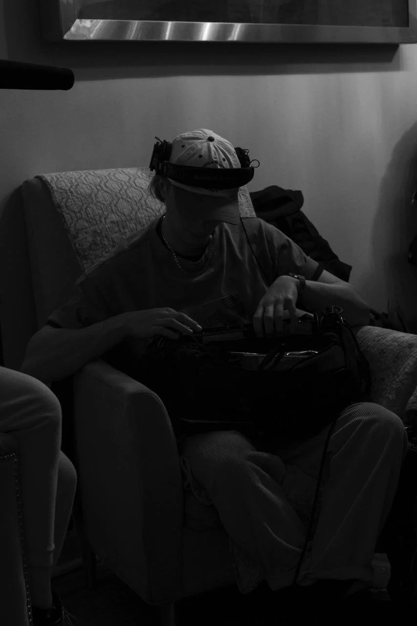 A person sitting on a chair with a quilted cover, wearing a cap and headphones, looking to a sounddevices mixer.