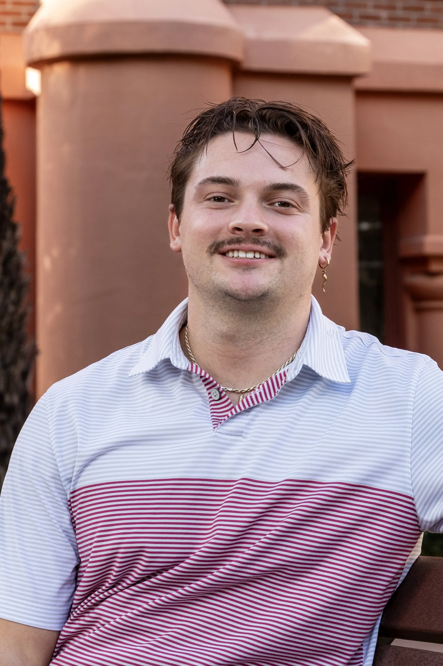 A young man with dark hair and a beard smiling outdoors