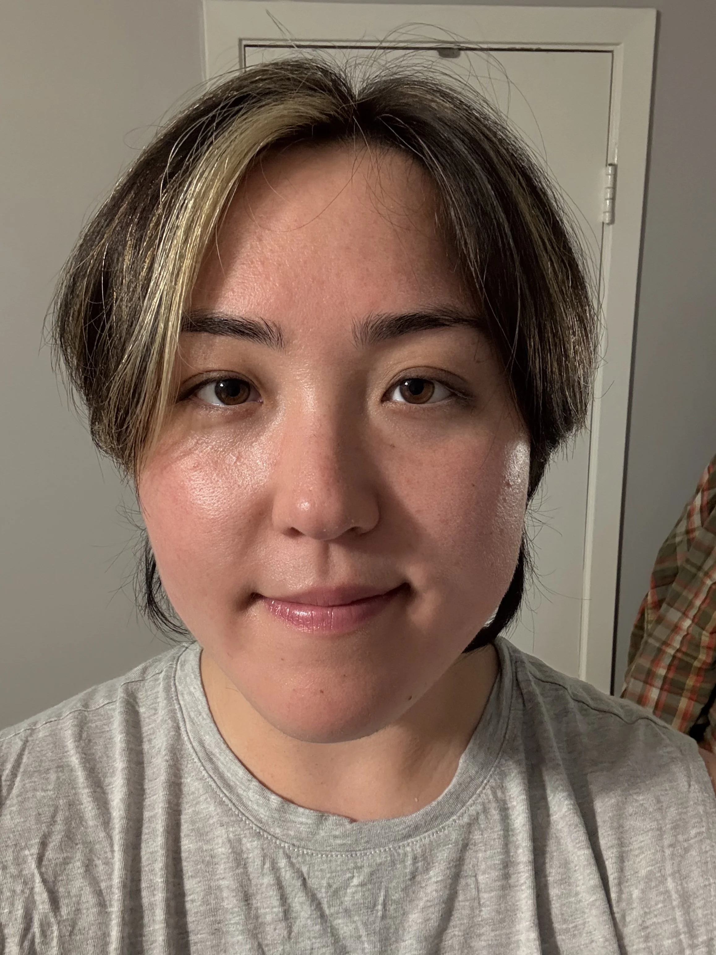 A man with curly dark hair, glasses, and a beard, wearing a black sweater, sitting indoors with a neutral background and a plant in the distance.