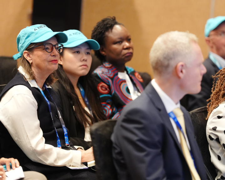 Group of diverse people sitting and listening at an event, some wearing blue caps and lanyards.