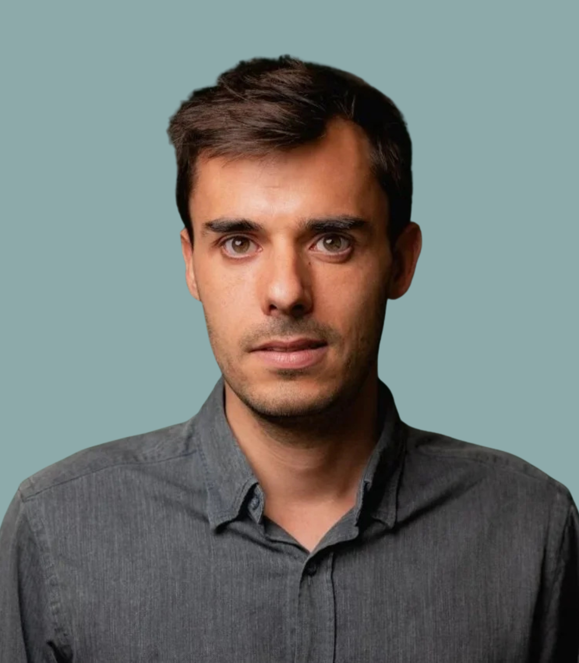 A portrait of Hugo, wearing a dark gray button-up shirt, against a teal background.