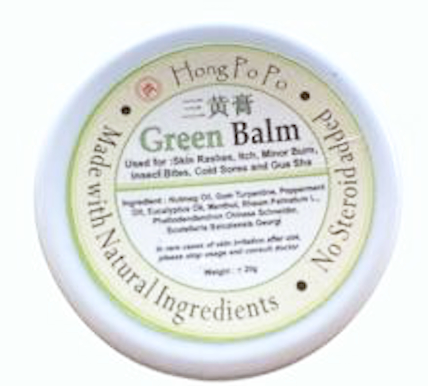 Close-up of a round container labeled 'Green Balm' with ingredients listed, marketed for skin health, made in Hong Kong.