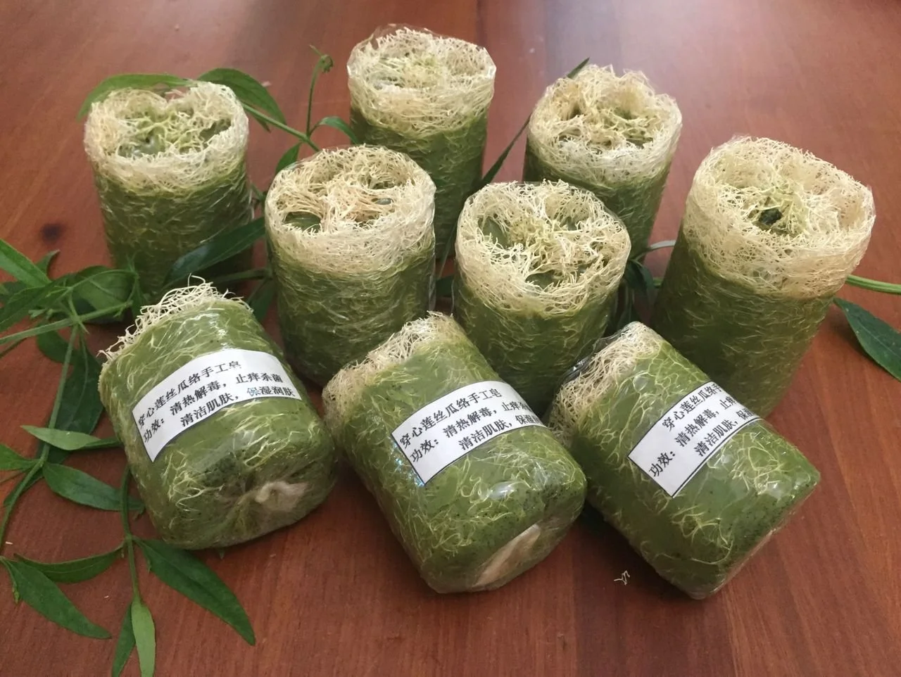 Multiple rolls of herbal soap with Chinese labels arranged on a wooden table, with green leaves around them.