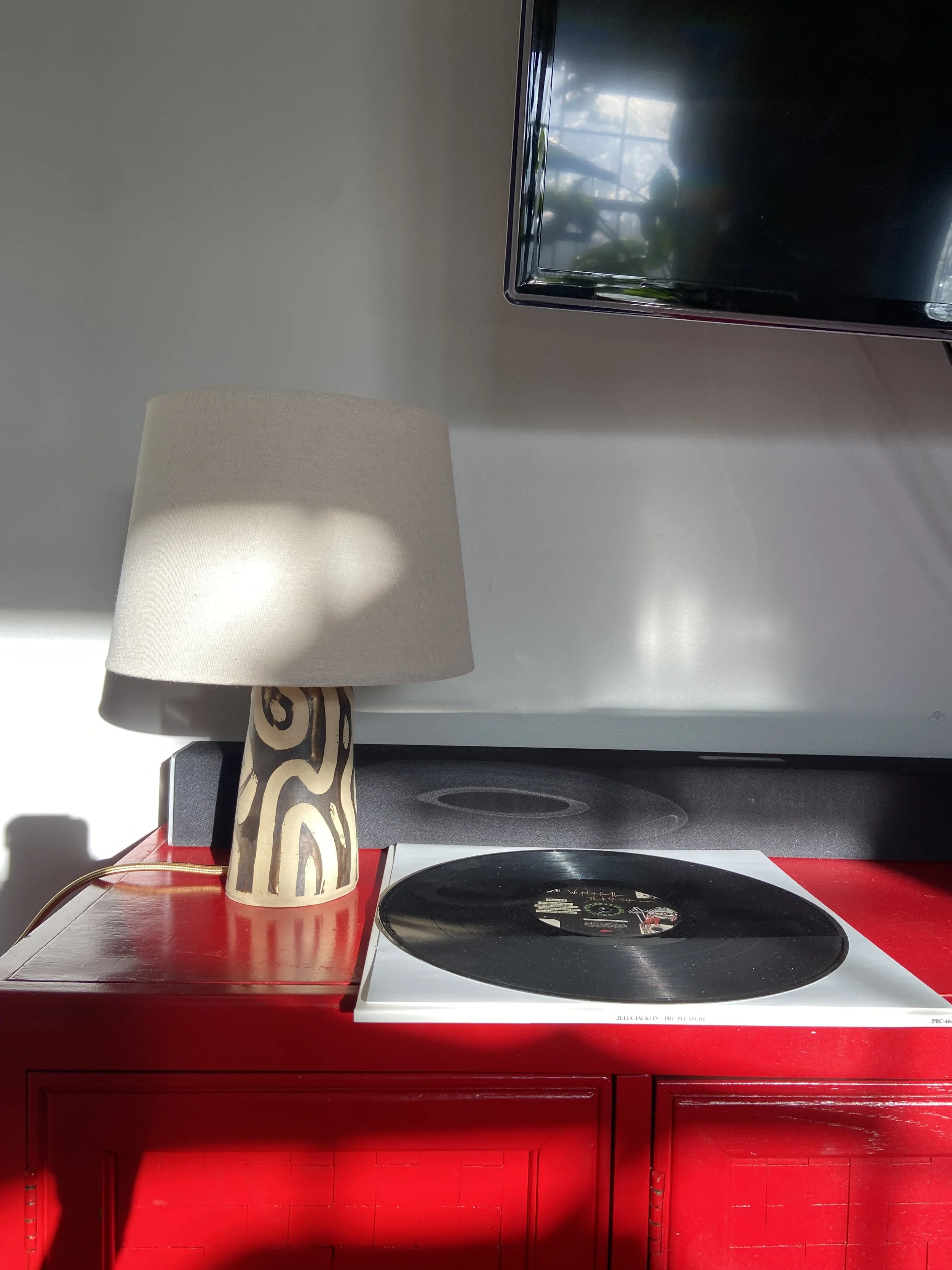 A red cabinet with a turntable record player, a lamp with a patterned shade, and a TV mounted on the wall above.