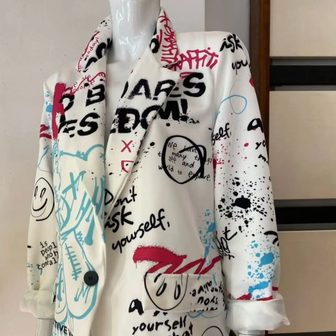 A cream-colored blazer covered in graffiti-style text, drawings, and splatters in black, red, and blue, displayed on a mannequin.