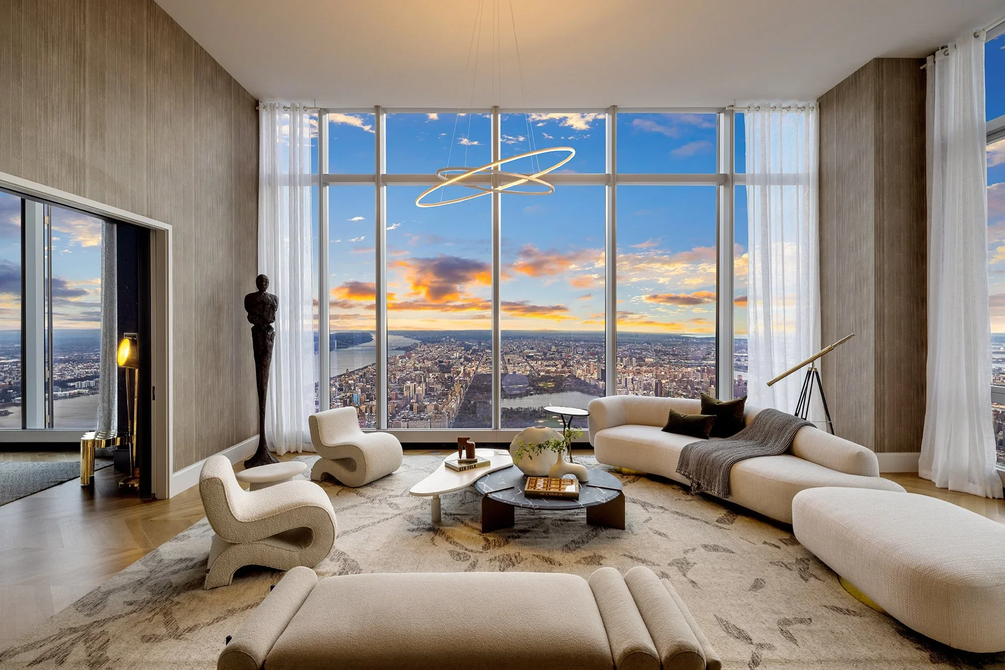 Modern high-rise apartment living room with large windows showing city skyline and river at sunset, featuring white sofas, contemporary chairs, a coffee table, and stylish decor.