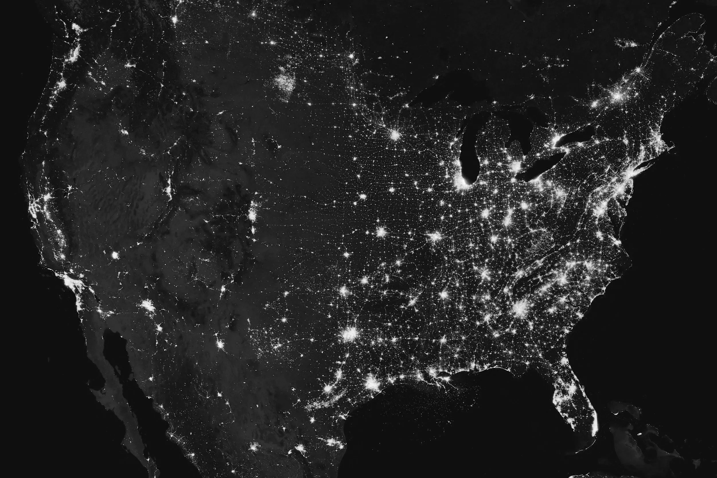 Satellite view of the United States at night showing illuminated cities and highways.