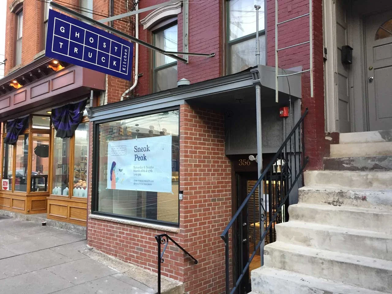 Street view of a brick building with a restaurant entrance, a sign that reads 'GHOST TRUCK Kitchen,' and a window with an advertisement for a sneak peek event at a restaurant.
