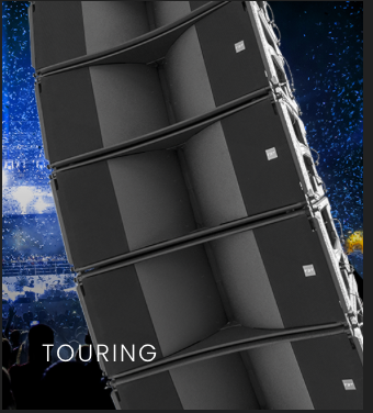 Large black tour speaker array with multiple connected speakers set against a nighttime city skyline with stars.