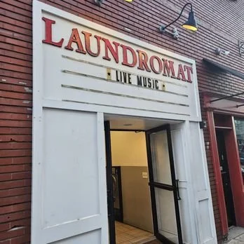 Entrance to a laundromat with a sign reading 'LAUNDROMAT' and 'LIVE MUSIC' on the building exterior.