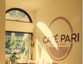 Interior of Café Pari with large window, decorative plants, and signage on the wall.
