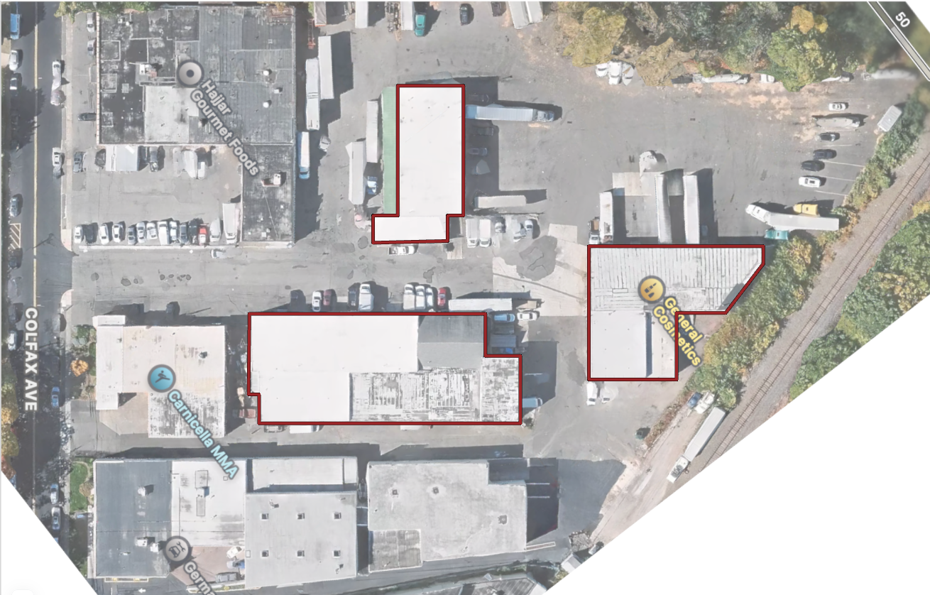Satellite view of a commercial area with multiple buildings outlined in red, parking lots, and surrounding streets labeled Colefax Ave and a railway track. Several parking spots along with store signs, including 'Gourmet Foods,' 'Canicella MMA,' and 'Gelosmetics,' are visible.