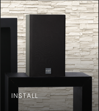 A large black speaker on a black table against a white brick wall.