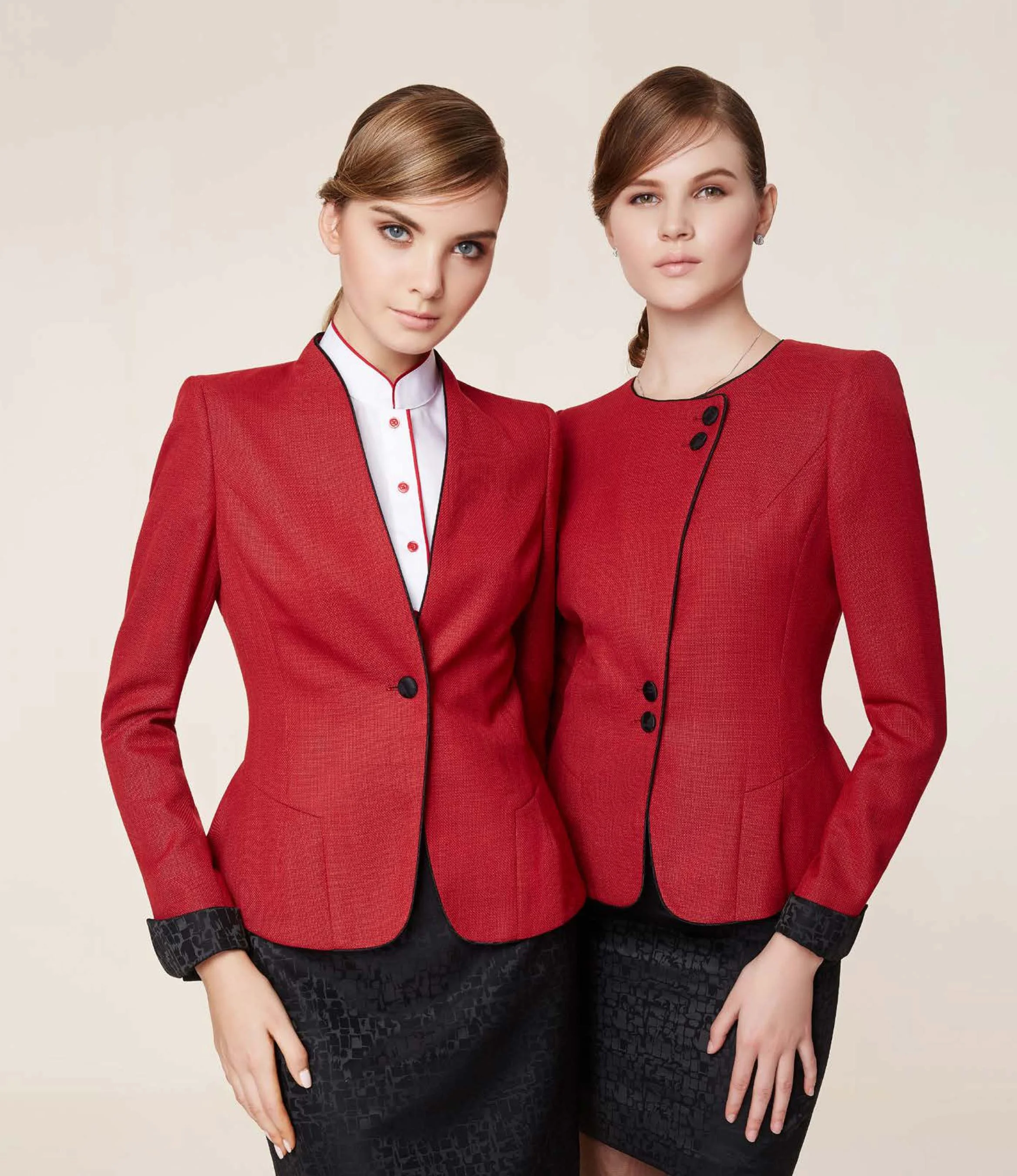 Two women wearing matching red blazers and black skirts standing side by side against a plain background.