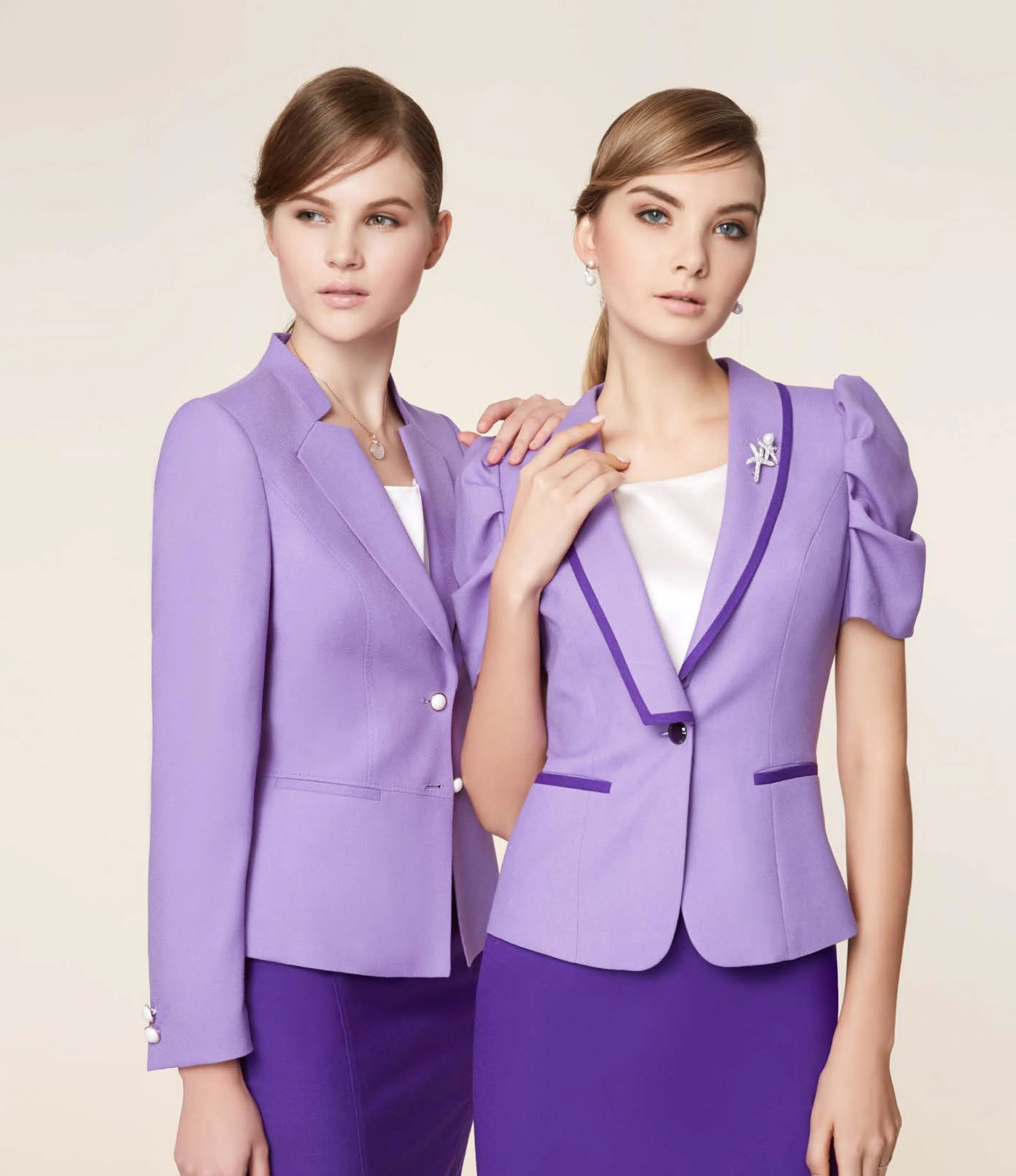 Two women wearing matching purple business suits and skirts posing against a plain background.