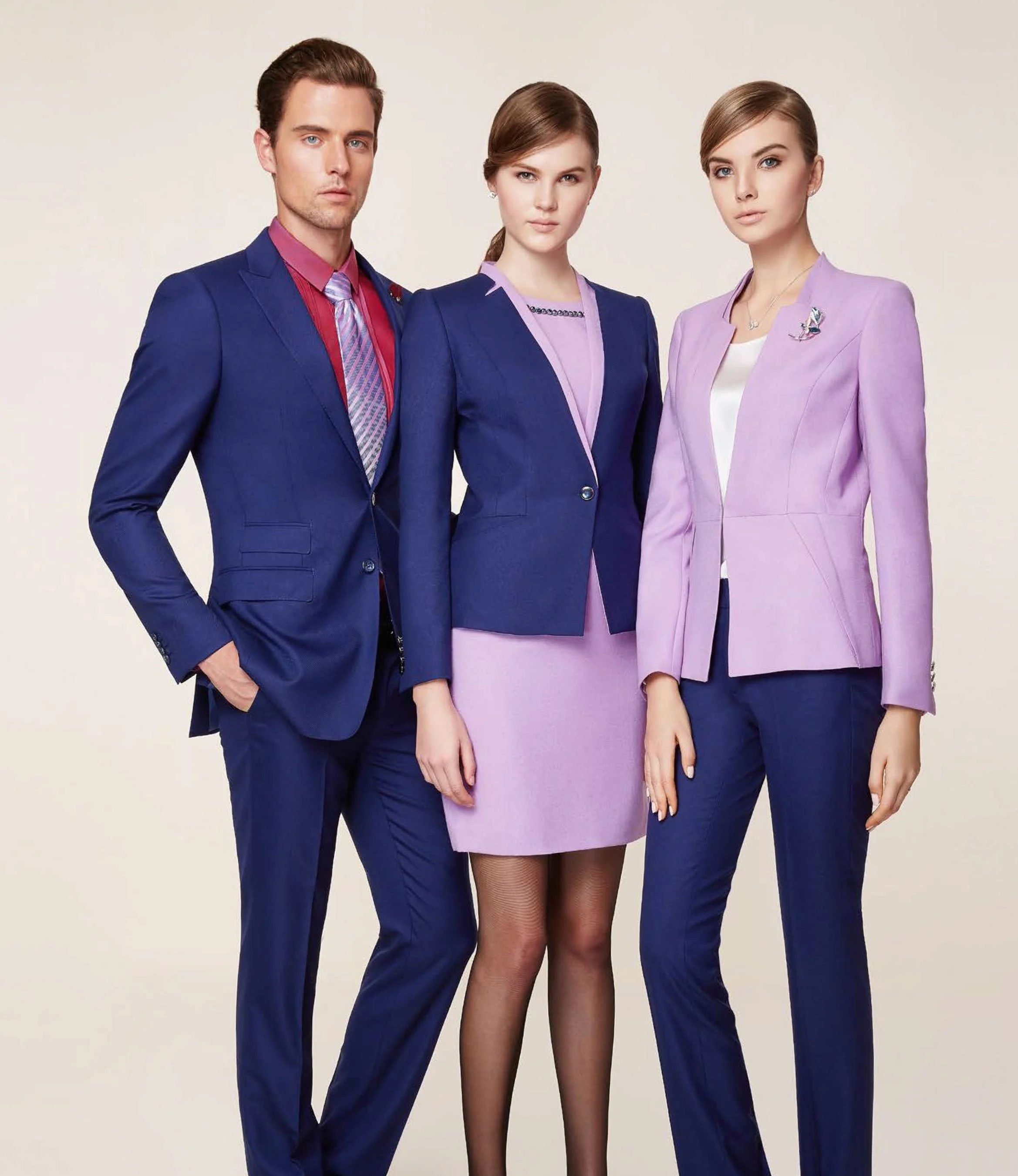 Three professionally dressed people standing side by side against a plain background, wearing business suits in shades of blue and pink.