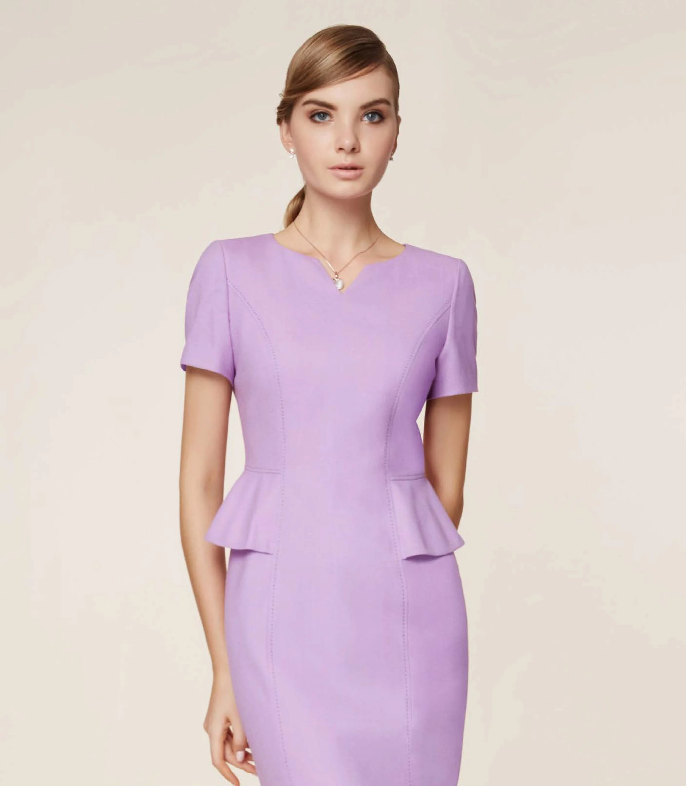 A woman wearing a lavender dress with short sleeves and a peplum detail at the waist, standing against a plain beige background.