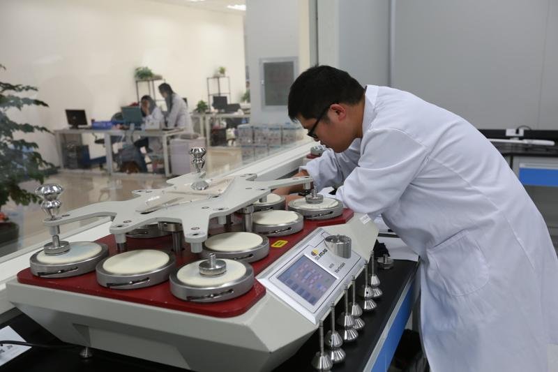Technician in white lab coat working with specialized industrial equipment in a modern laboratory.