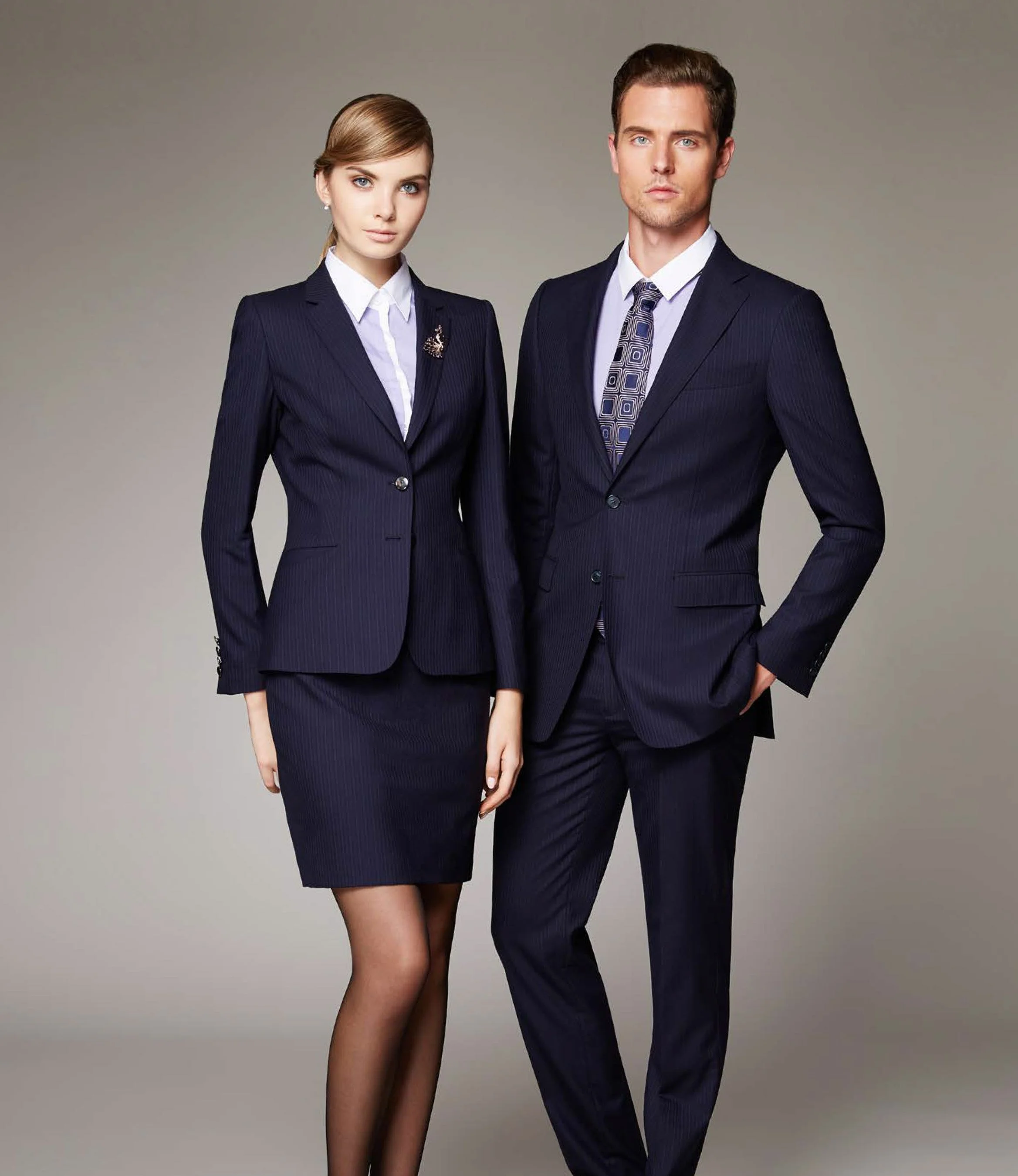 A man and woman dressed in formal navy blue business suits with white shirts posed against a plain background.