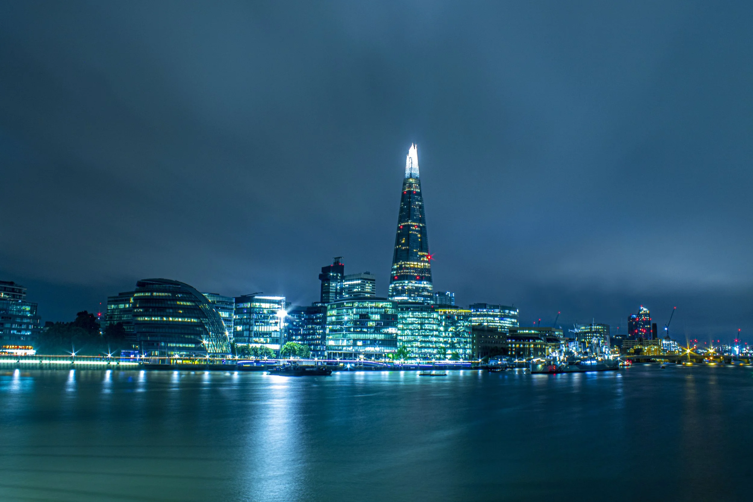 Night view of the London skyline featuring The Shard illuminated, with surrounding modern buildings along the river.