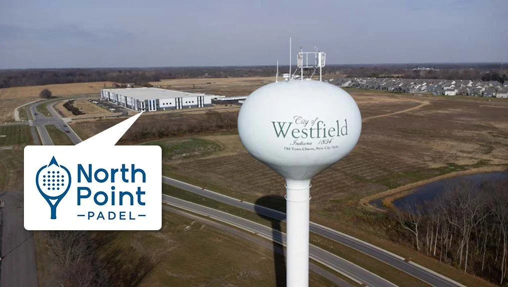 Water tower with 'City of Westfield, Indiana 1880, Old Town Charm, New City Style' written on it, adjacent to a North Point Padel logo, surrounded by roads, open land, and a small pond.