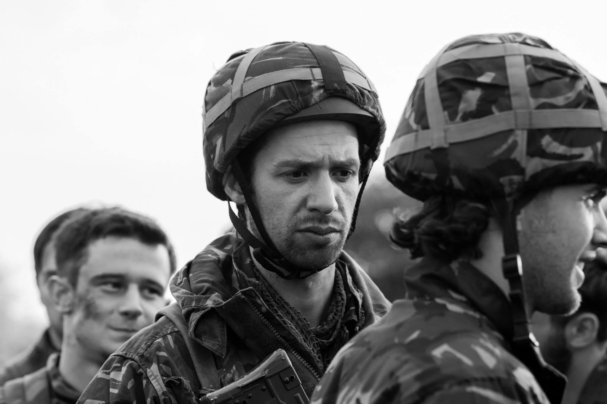 Black and white photo of a group of soldiers wearing camouflage uniforms and helmets, standing outdoors in formation.