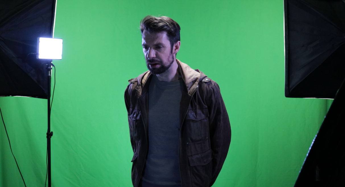 Man standing in front of a green screen, surrounded by studio lighting equipment.