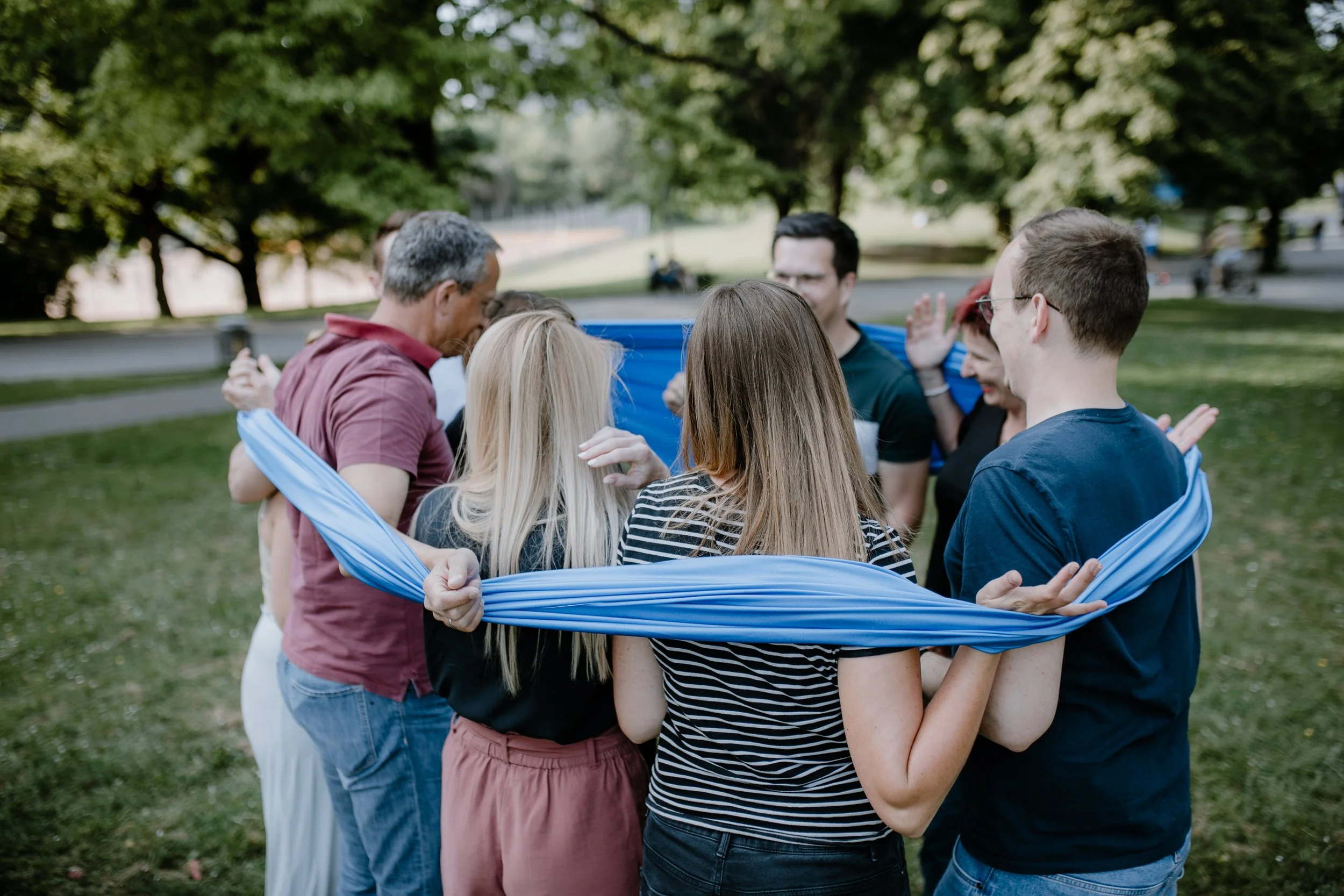 Gruppe von Menschen steht im Kreis im Park, umarmt sich und lacht.