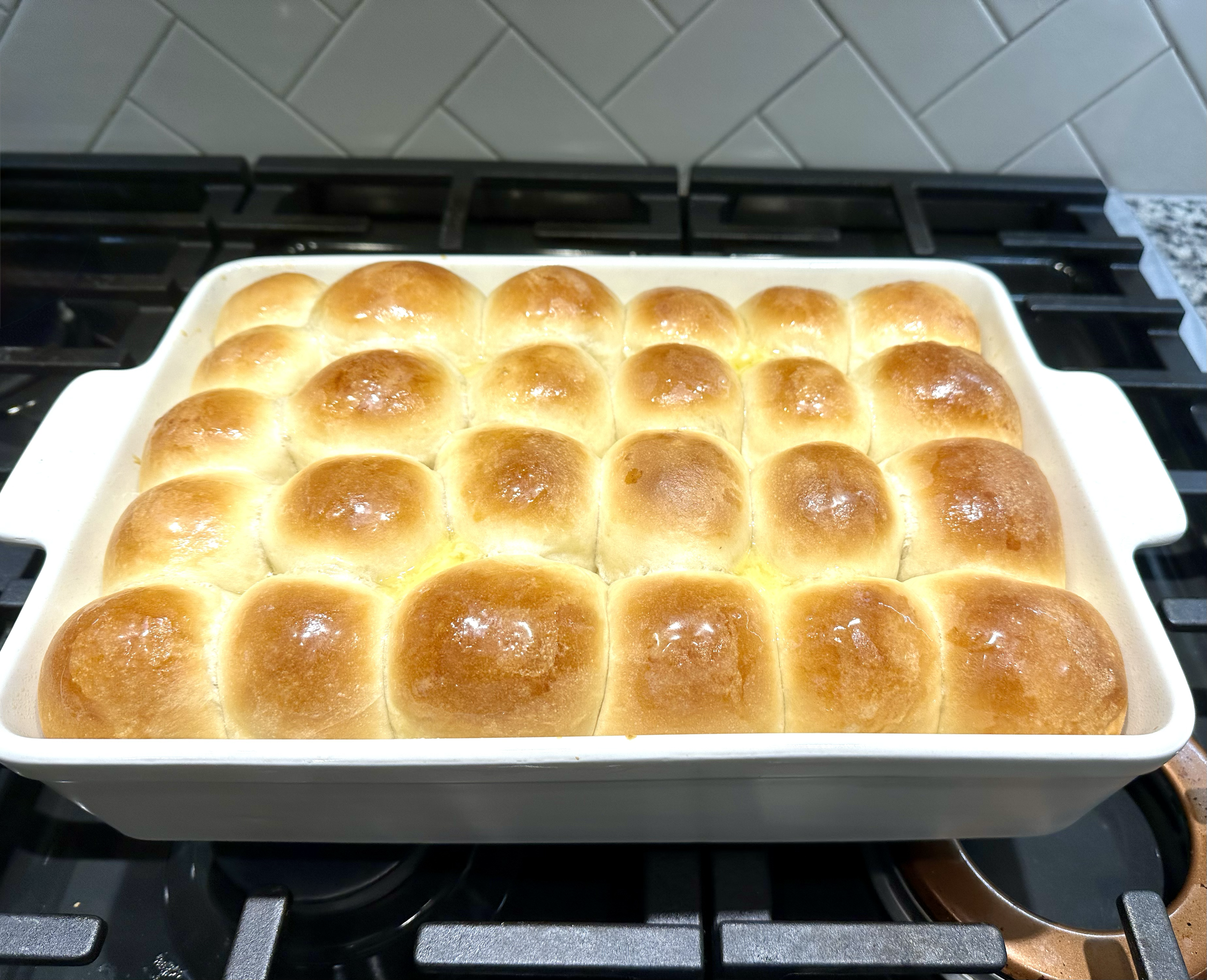 Baked dinner rolls in a white baking dish on a stovetop.