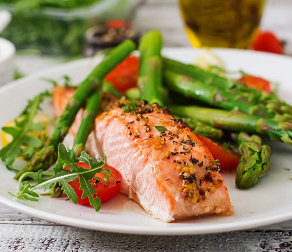 Cooked salmon fillet with pepper and herbs, served with asparagus and cherry tomatoes on a white plate.