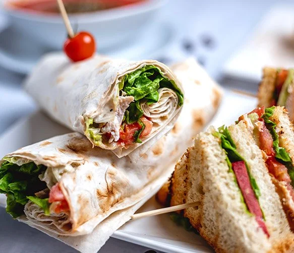 Chicken wrap with lettuce and tomatoes on a white plate, with sandwich cut into halves with lettuce, tomato, and meat inside.