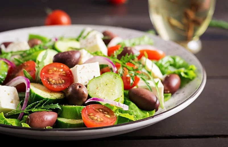 Fresh vegetable salad with cherry tomatoes, cucumbers, Kalamata olives, red onions, lettuce, and feta cheese on a white plate