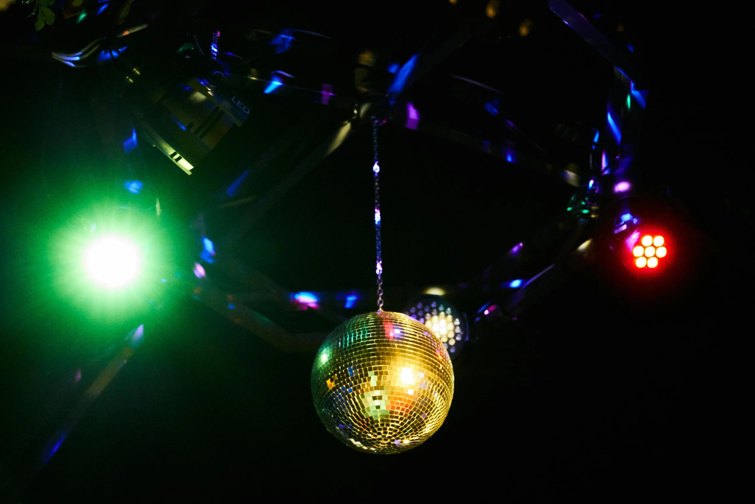 A mirror ball hanging from the ceiling reflecting colorful lights in a dark setting, creating a festive atmosphere.