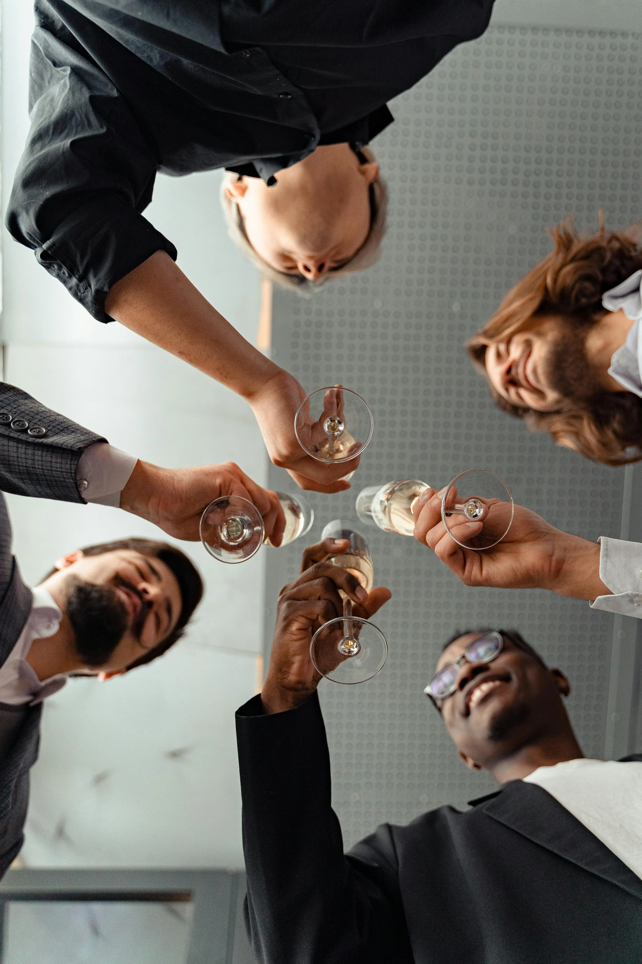 Group of five people holding glasses of champagne in a toast, seen from below.