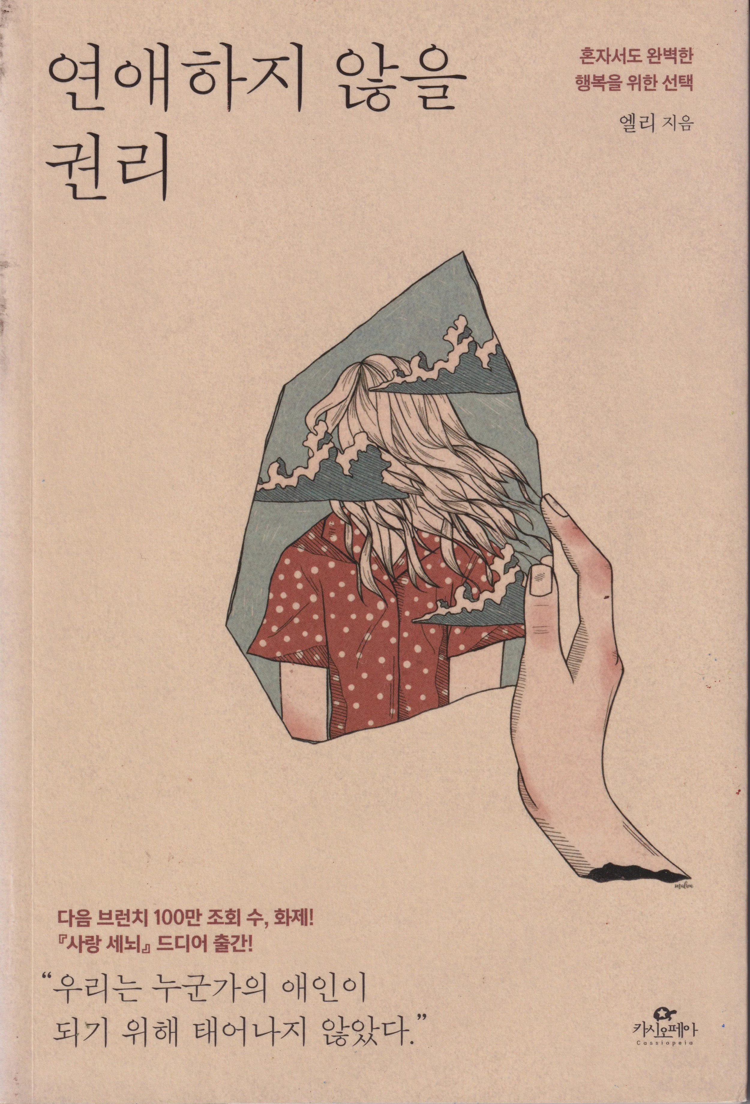 Korean book cover with illustration of a hand holding a photograph of a woman with long, wavy hair wearing a red polka dot shirt, the image showing mountains and clouds above her head.