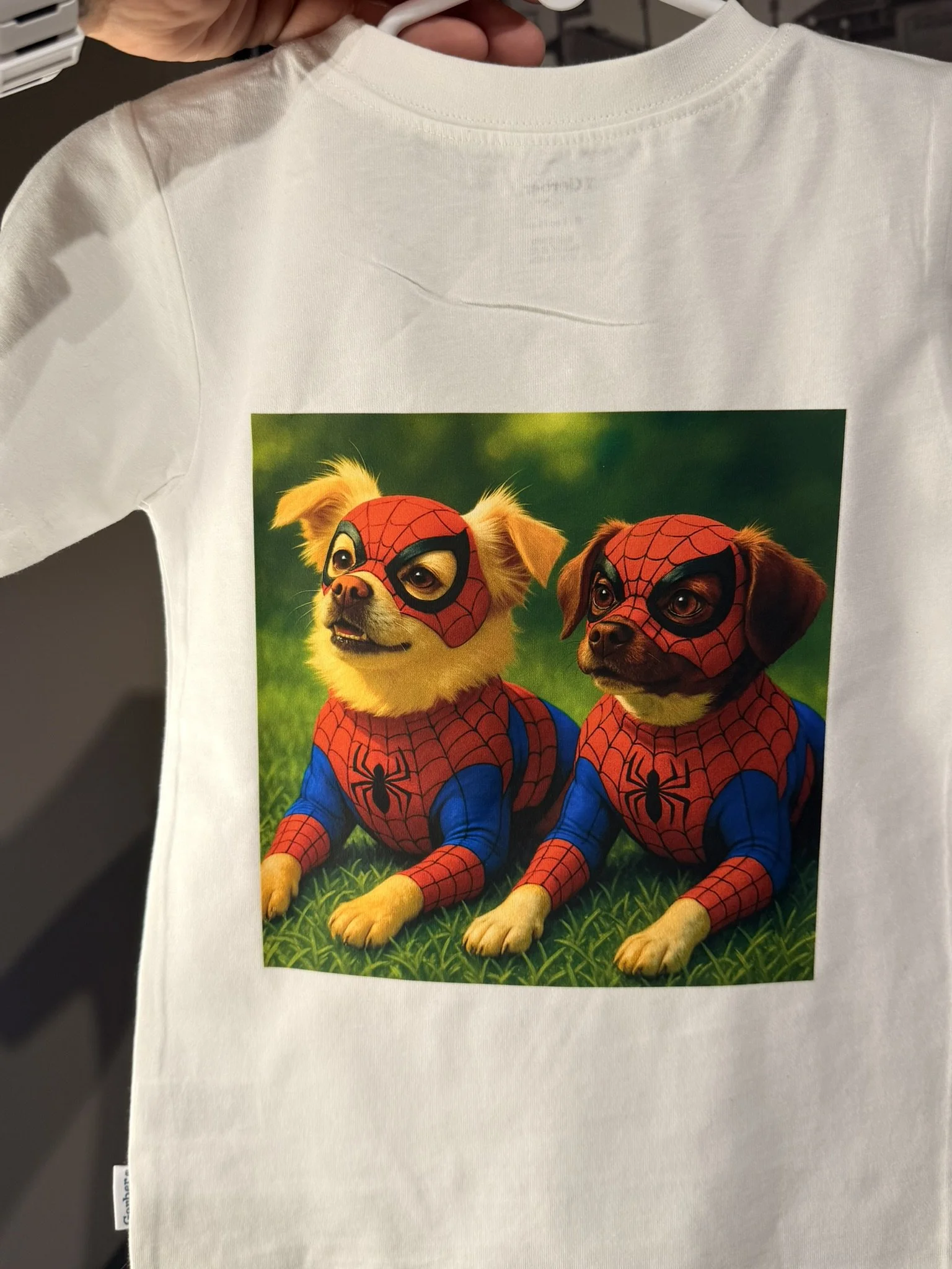 White T-shirt with a printed photo of two dogs dressed in Spider-Man costumes, sitting on grass with a blurred green background.
