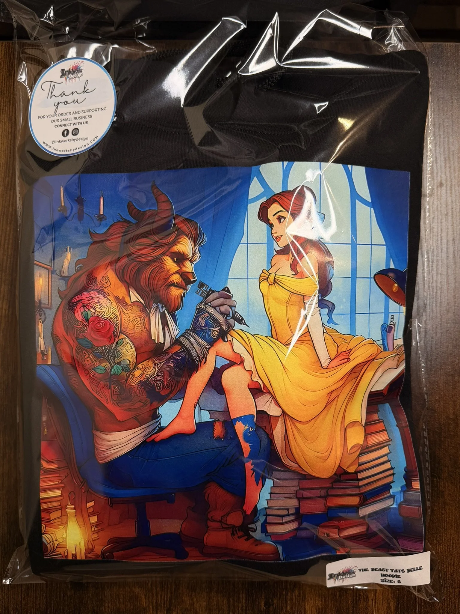Colorful illustration of a beast and Belle from Beauty and the Beast in a tattoo-style art, with the beast tattooed and Belle sitting on a stack of books in a room with blue curtains and warm lighting.