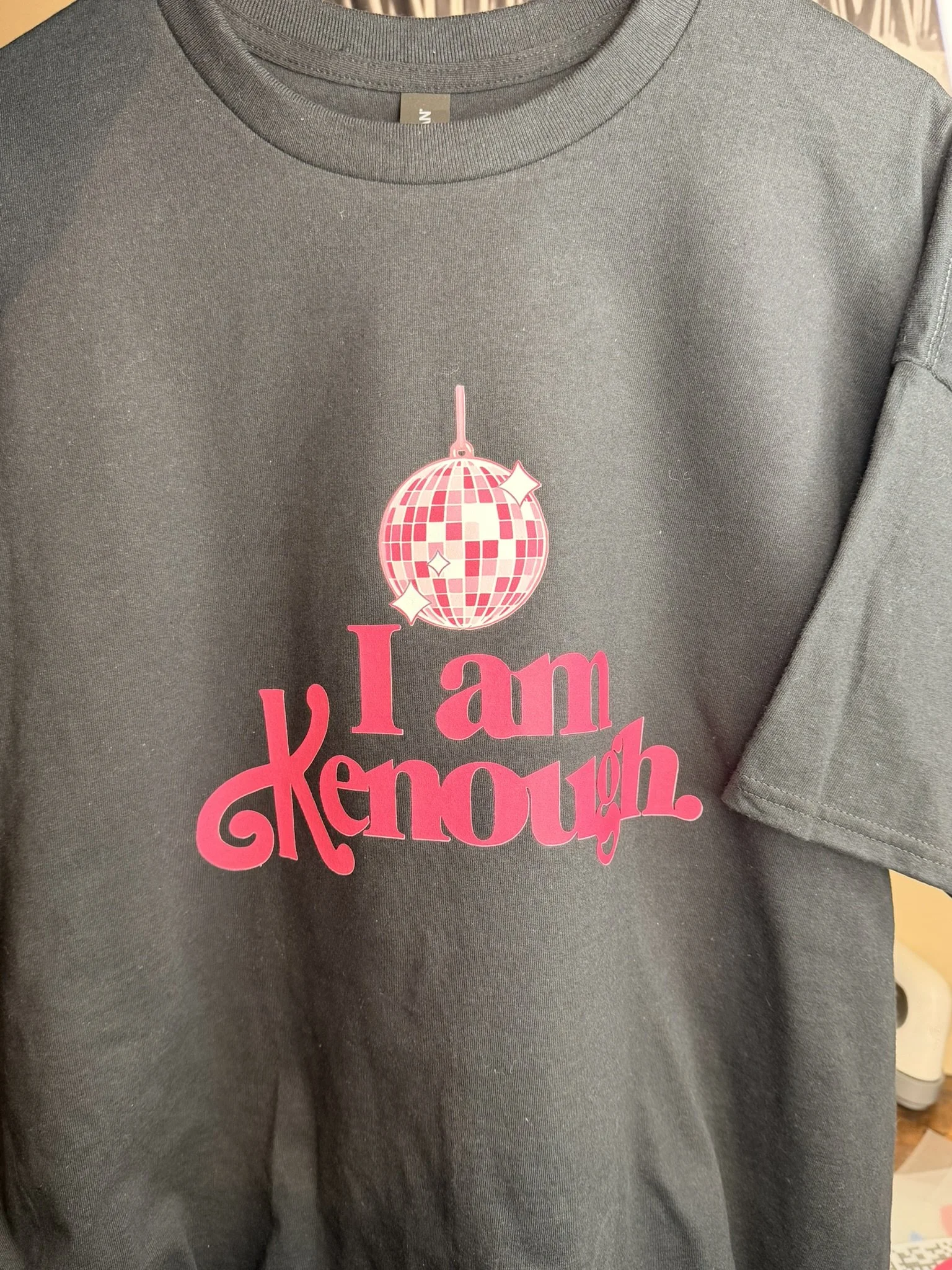 Gray T-shirt with pink text and graphic design. The text says 'I am known' in large, stylized letters. Above the text, there is a pink disco ball graphic.
