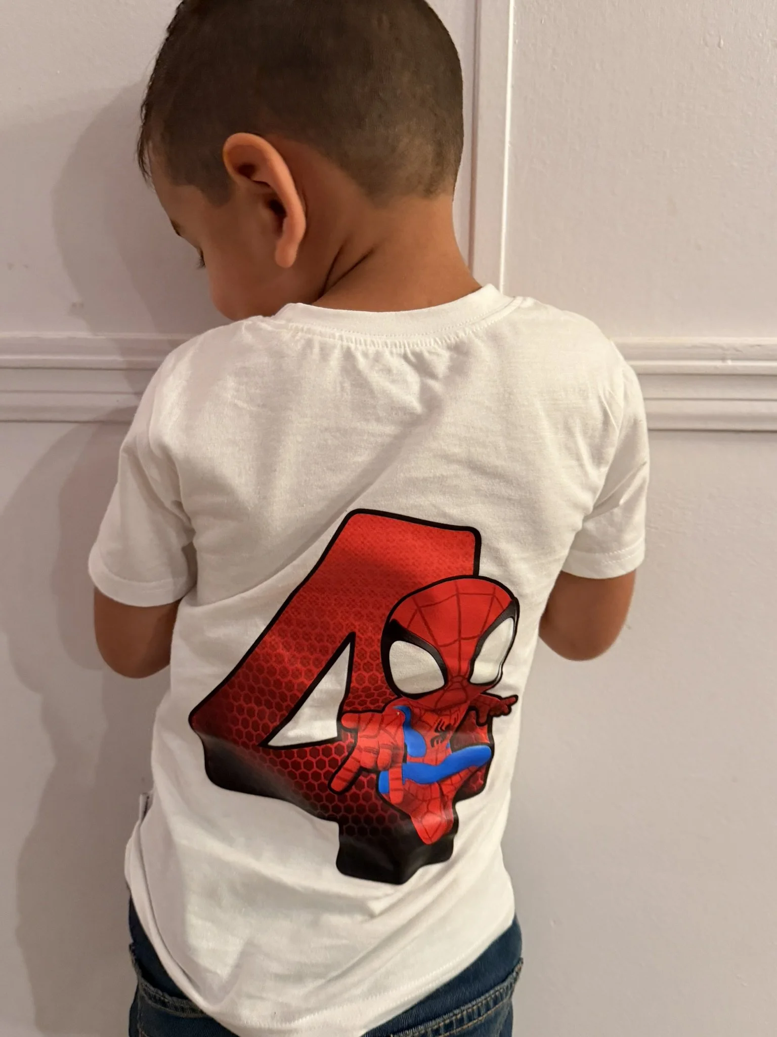A young boy wearing a white T-shirt with a large red number 4 and a Spider-Man graphic on the back.
