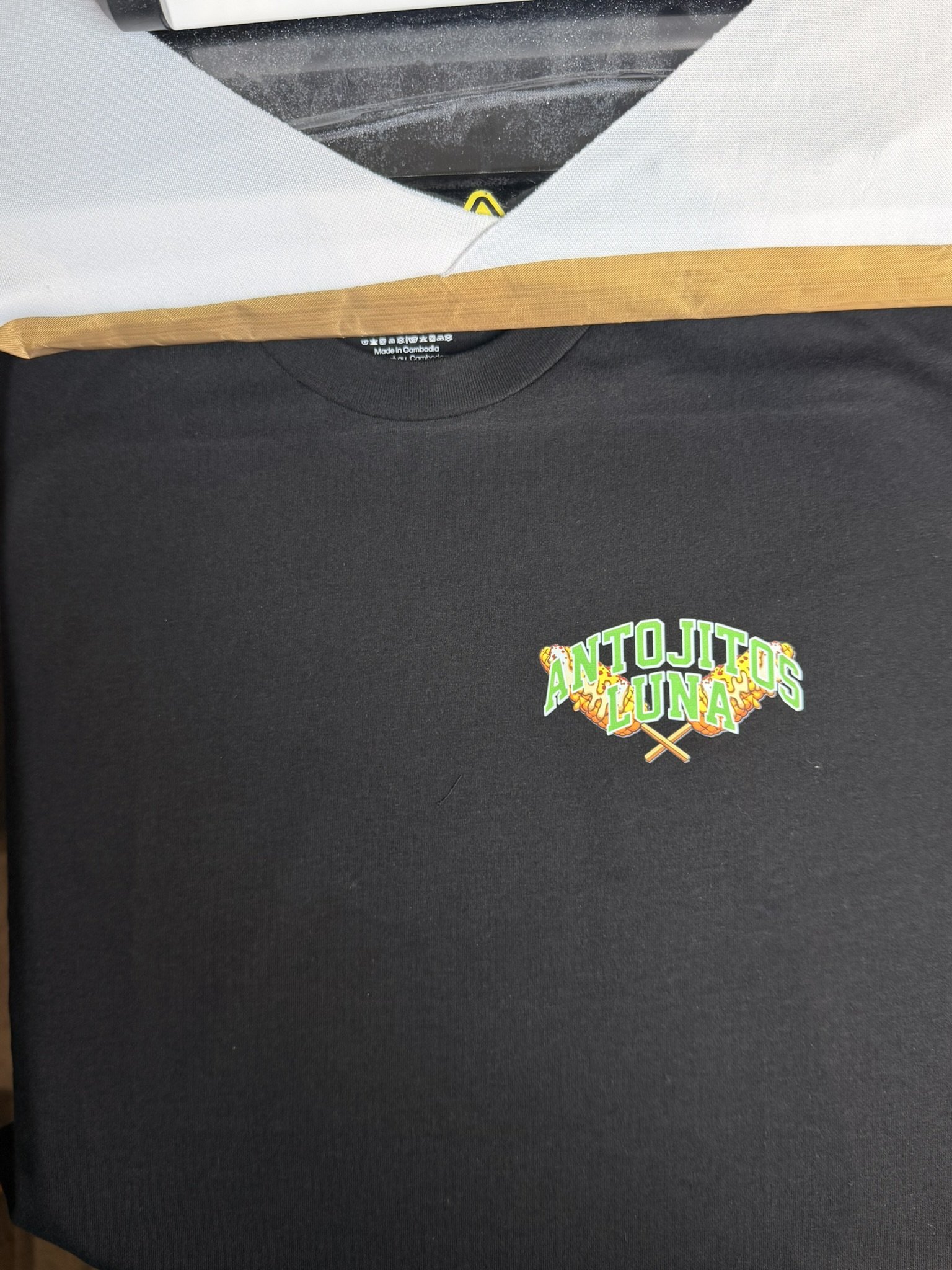 Black T-shirt with a colorful comic-style logo that reads "ANTO JITOS LUNA" with crossed skewers beneath the text.