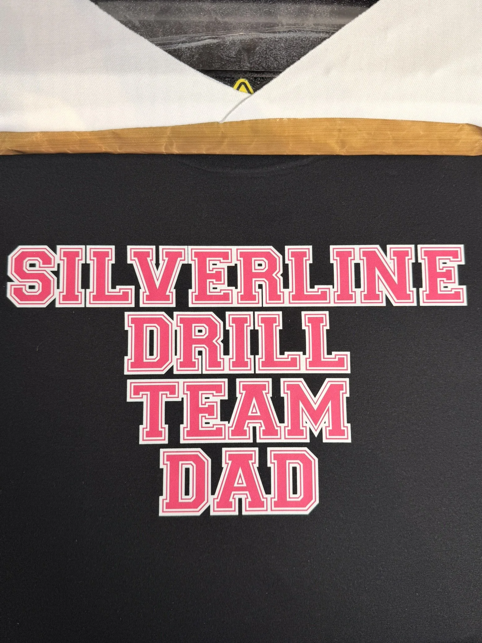 A sticker on a black surface with bold pink and white text that reads "Silverline Drill Team Dad."