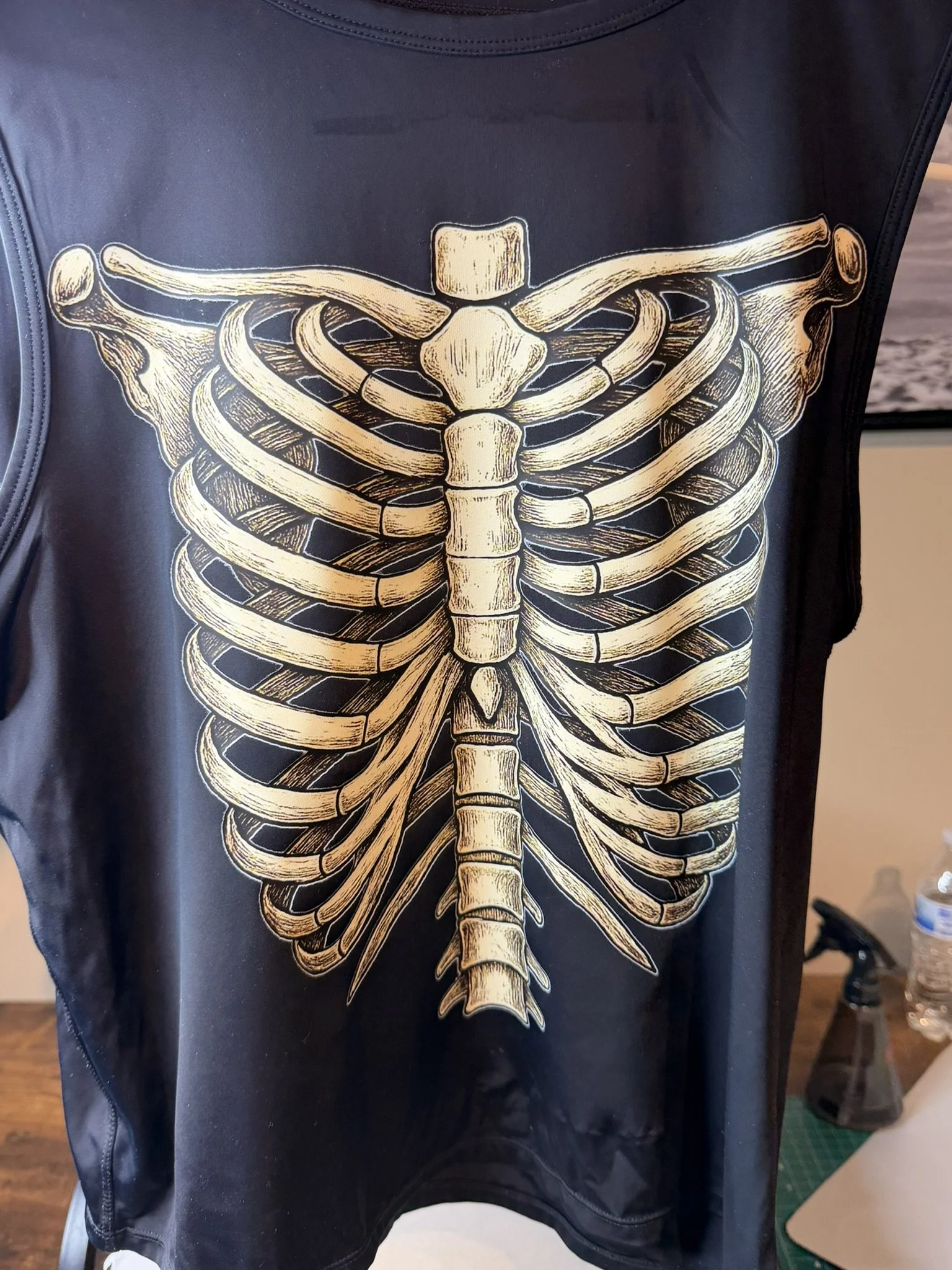 A black fabric with a large, detailed illustration of a human skeleton's ribcage, spine, and wings printed in gold.