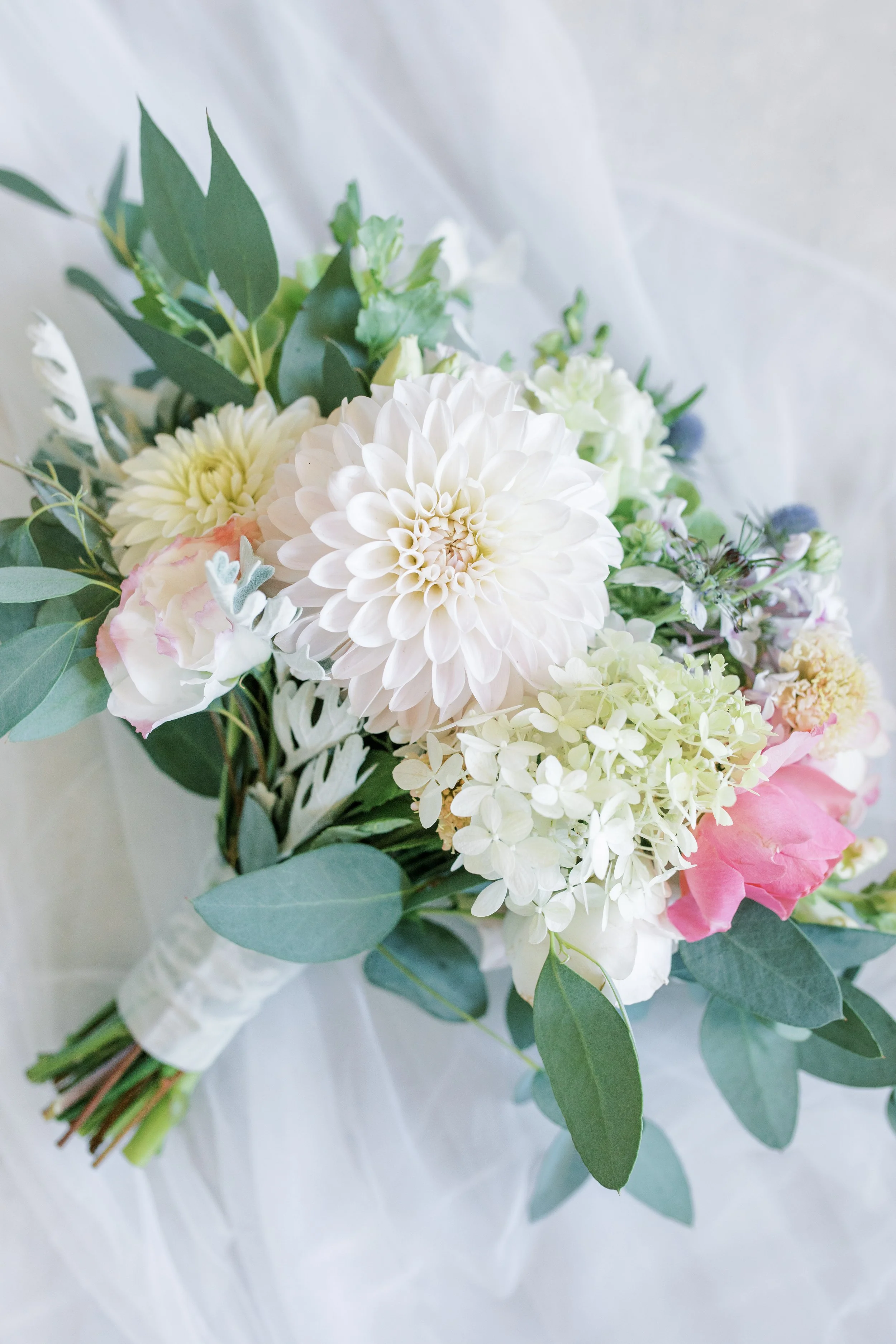 A bouquet of white, pink, and cream-colored flowers with green leaves on a white background. Photo by McKenna Rachelle Photgraphy