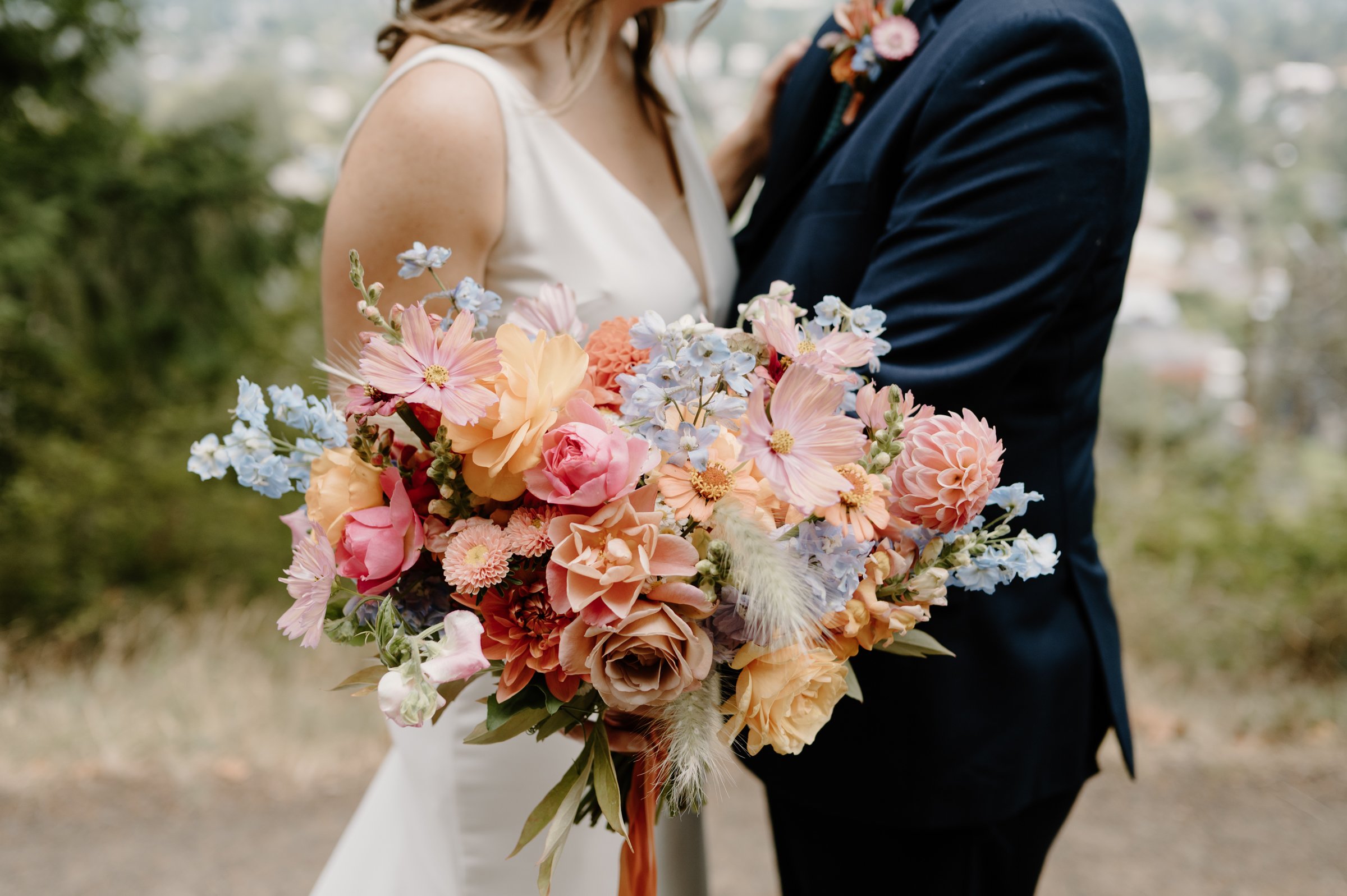 A bride and groom holding a large bridal bouquet of colorful flowers outdoors.

Photo by Mackenzie Hughes Photography