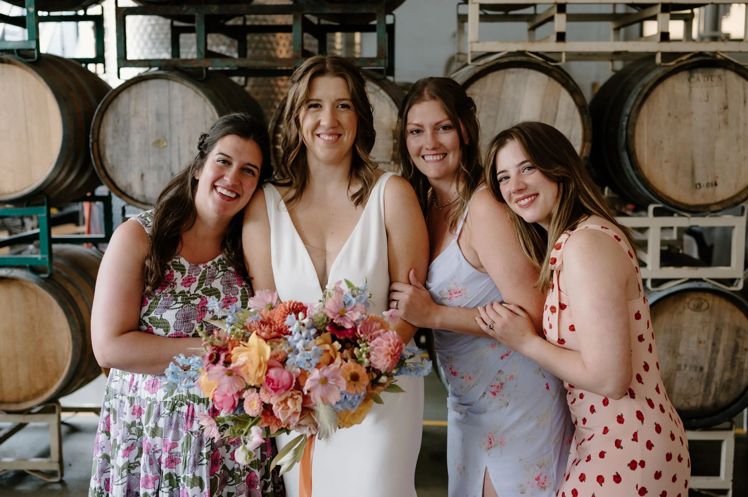 Four women at a winery, a bride in a white wedding dress holding a bouquet, surrounded by her bridesmaids in mismatched floral printed dresses and wine barrels in the background.

Photo by Mackenzie Hughes Photography
Venue: Cooper's Hall in SE Portl