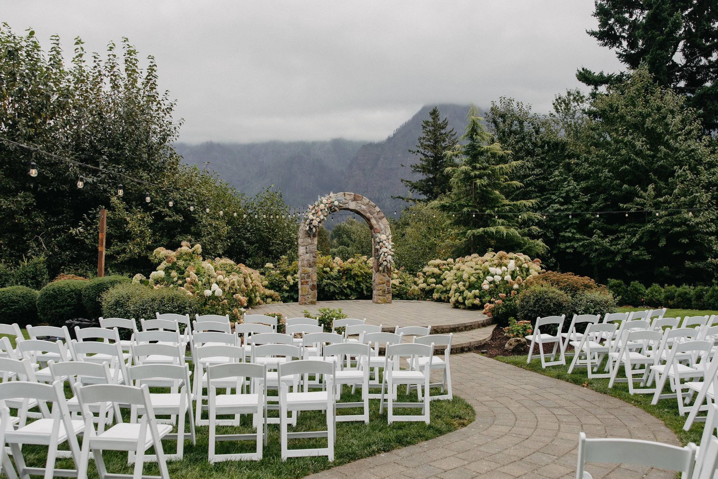 Outdoor wedding ceremony setup with rows of white chairs facing a stone arch with flowers, surrounded by greenery and mountains.

Photo by Go Lovin Co Photography
Venue Cape Horn Estates